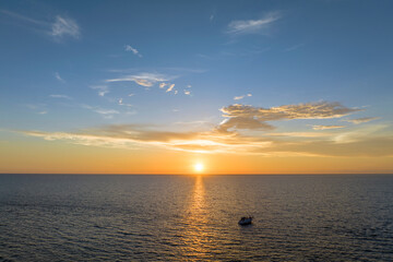 Aerial view of unrecognizable people having fun on white yacht at sunset floating on sea waves with ripple surface. Motor boat recreation on ocean surface