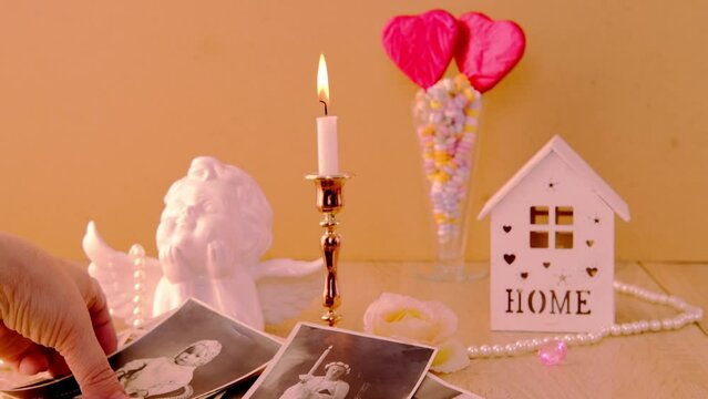 close-up female hand holding old vintage photos, romantic still life in love style, in vase red hearts on sticks, candles burning, cupid, concept of family tree, genealogy, childhood memories