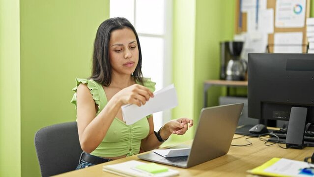 Young beautiful hispanic woman business worker using laptop reading letter looking upset at office