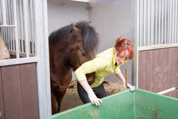 Horses paddock cleaning hygiene, excrement for eco-friendly fertilizer. Middle-aged Hispanic woman