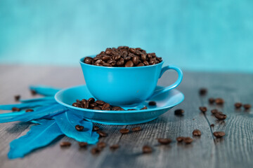 Coffee beans in blue coffee cup and saucer coffee beans scattered blue background