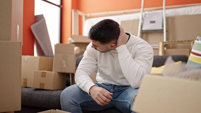Young hispanic man stressed sitting on sofa at new home