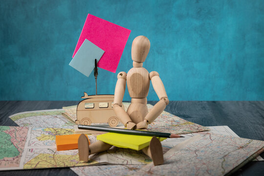 Wooden mannikin holding a pencil sitting on Road maps blank signs In background 
