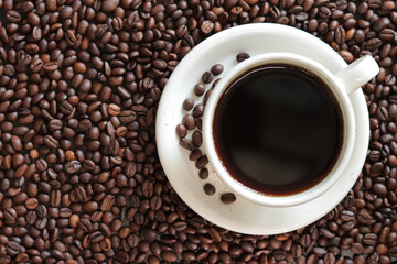 A cup of black coffee with scattered roasted coffee bean, top view. Americano coffee. Top view of a cup of coffee on the background of roasted coffee beans