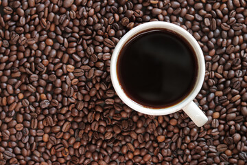 A cup of black coffee with scattered roasted coffee bean, top view. Americano coffee. Top view of a cup of coffee on the background of roasted coffee beans