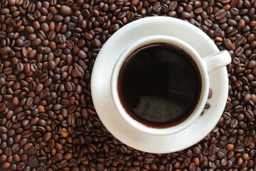 A cup of black coffee with scattered roasted coffee bean, top view. Americano coffee. Top view of a cup of coffee on the background of roasted coffee beans