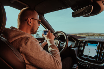 A tired man drinking acoffee while driving a car at sunset. Tired travel and long drive