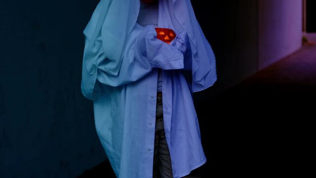 ghost child 10 years old in white hoodie holds pumpkin candle in hands in creepy tunnel, sad boy ghost night, halloween festival concept, frightening mystical events, friday 13th, horror movie scene