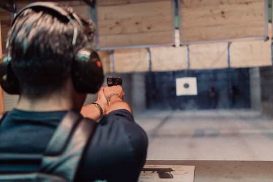 A man practices shooting a pistol in a shooting range while wearing protective headphones