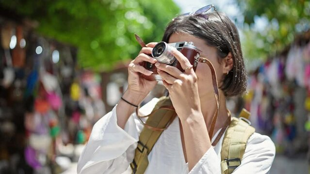 Young beautiful hispanic woman tourist smiling confident using vintage camera at street market