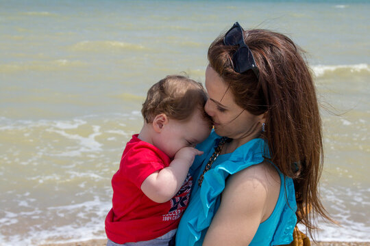 Image of a young mother by the sea hugging and kissing her little son. Maternal love during a beach holiday in Italy
