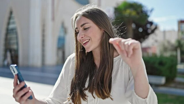 Young beautiful hispanic woman dancing listening to music on smartphone at street