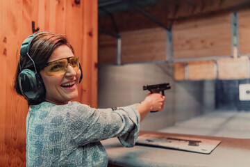 A woman practices shooting a pistol in a shooting range while wearing protective headphones