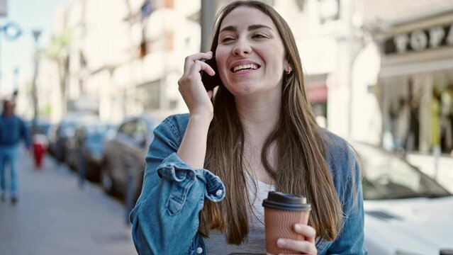 Young beautiful hispanic woman talking on smartphone drinking coffee at street