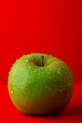 manzana verde con gotas de agua sobre fondo rojo