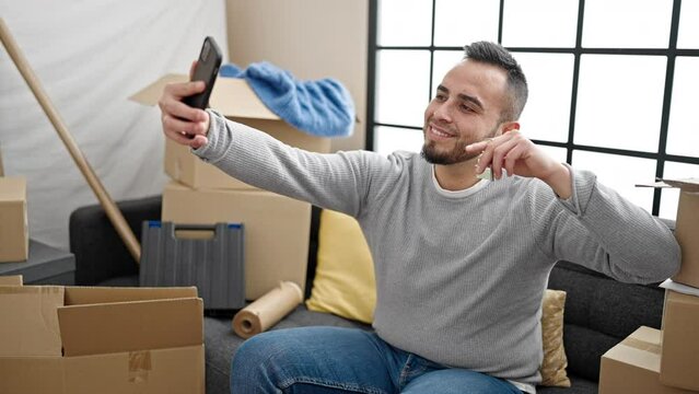 Hispanic man sitting on the sofa taking a picture showing keys at new home