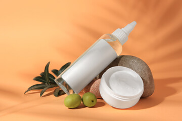 Cosmetic products and olives on orange background