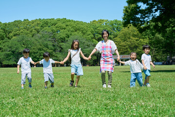 Fototapeta premium 緑地で手を繋いで並ぶ子どもたちと女性