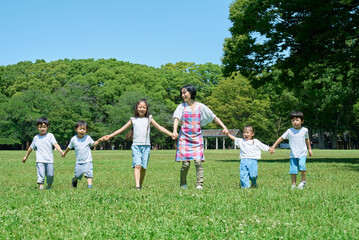 Fototapeta premium 緑地で手を繋いで並ぶ子どもたちと女性