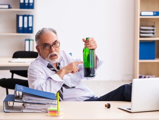 Old male employee drinking alcohol in the office