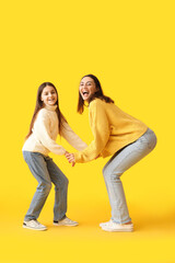 Fototapeta premium Little girl and her mother in knitted sweaters dancing on yellow background