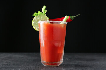 Glass of bloody mary cocktail garnished with cilantro, lime and red chili pepper on dark background