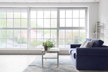 Interior of light living room with cozy blue sofa and modern laptop on table near big window