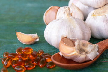 Garlic bulbs, capsules of oil extract, garlic cloves on wooden spoon.
