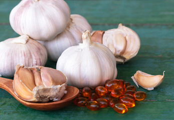 Garlic bulbs, capsules of oil extract, garlic cloves on wooden spoon.