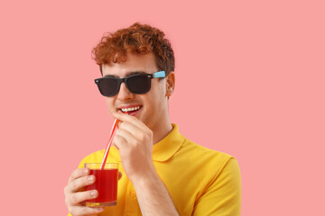 Young man drinking red juice on pink background, closeup