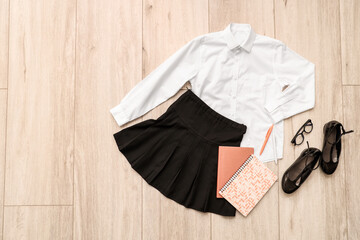 Composition with stylish school uniform, shoes, eyeglasses and stationery on wooden background