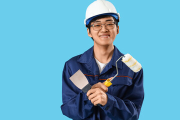 Asian decorator with putty knife and paint roller on blue background