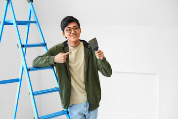 Young Asian man pointing at putty knife in room