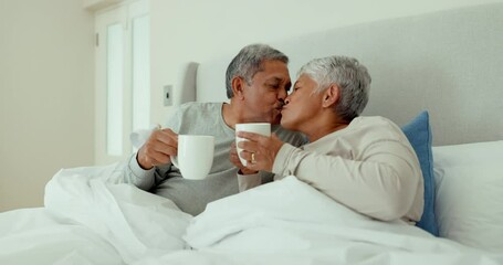 Couple, coffee and kiss in bedroom for love, care and quality time together on holiday, vacation or freedom of retirement. Senior man, happy woman and drinking tea for romantic morning, relax or home - Powered by Adobe