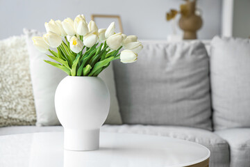 Vase with blooming white tulip flowers on coffee table in living room, closeup