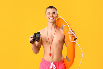 Male lifeguard with binoculars and ring buoy on yellow background