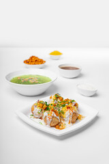 dahi puri or dahipuri a very spicy punjabi chat item on white plate with chutney and chilly water bowls, styling and garnished group shot