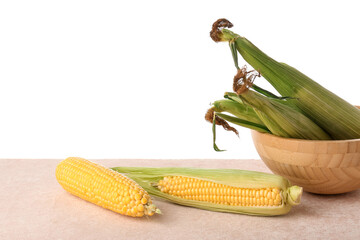 Bowl with fresh corn cobs on pink table against white background