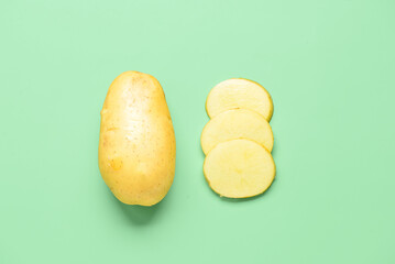 Whole and cut potatoes on green background