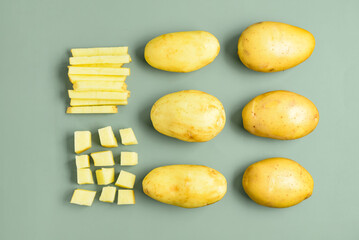 Whole and cut potatoes on green background