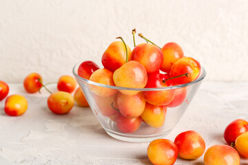 Glass bowl with sweet yellow cherries on white background