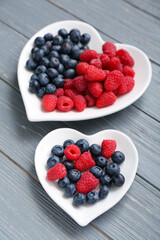 Plates with different fresh berries on grey wooden background, closeup