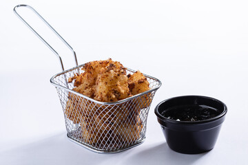 Porção de queijo à milanesa com molho, servida em um cesto de metal em um fundo branco