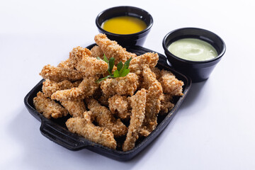 Porção de isca de frango frita com maionese temperada, servida em uma cumbuca preta, em um fundo branco