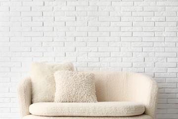 Cozy white sofa with pillows near brick wall
