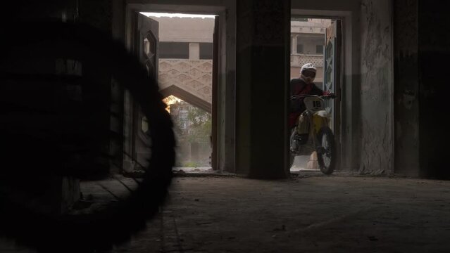 Two bikers on sports bikes and protective suits drive into a dark old building