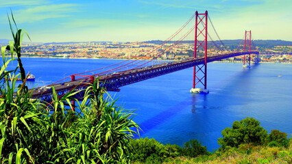  lange rote Hängebrücke über den blauen Fluss Tejo (Brücke des 25. April) in Lissabon mit grünem Busch 
