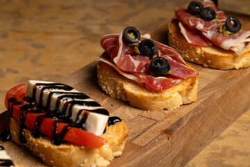 Sandwich made of bread, tomato, cheese, ham and olives. Served on a wooden plate in a restaurant