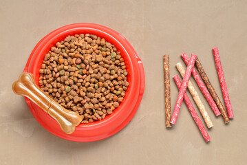 Bowl with dry dog food and treats on color background