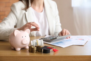 Woman in business suit sitting at table with stacks of coins, dollar banknotes and piggy bank. Student loan concept
